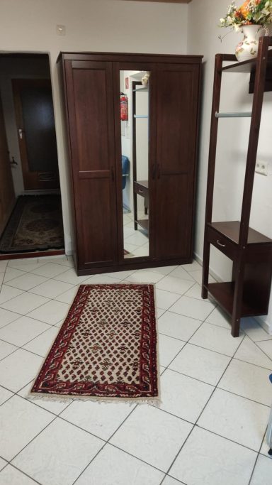 Heller Eingangsflur Holzschrank mit Spiegel in einem Raum, Teppich und Regal im Hintergrund.