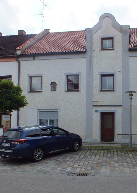 Zugang zum Gästehaus mit kostenlosen Parkplätzen Helles Gebäude mit grauer Fassade, einem Auto davor und einem Baum an der Seite.